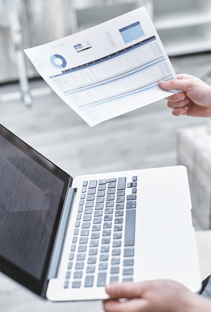 Person reviewing data on a laptop with a paper document in hand, emphasizing digital analysis.